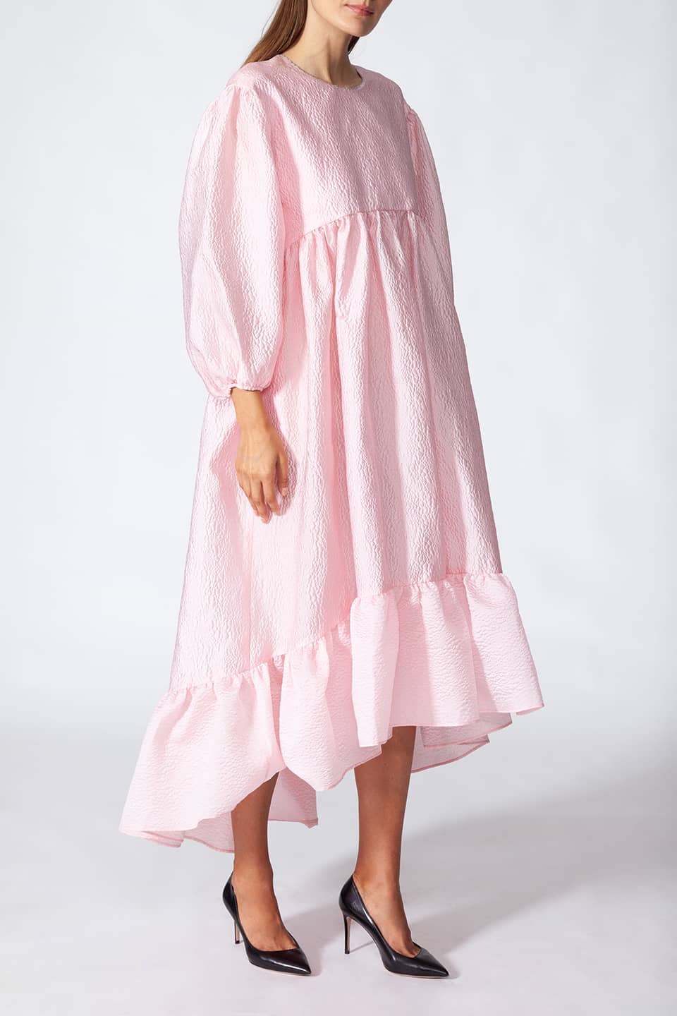 Model in pose from left side wearing Manoush sylist pink long dress with puffy sleeves. Scalloped neck with contrasting stitching.
