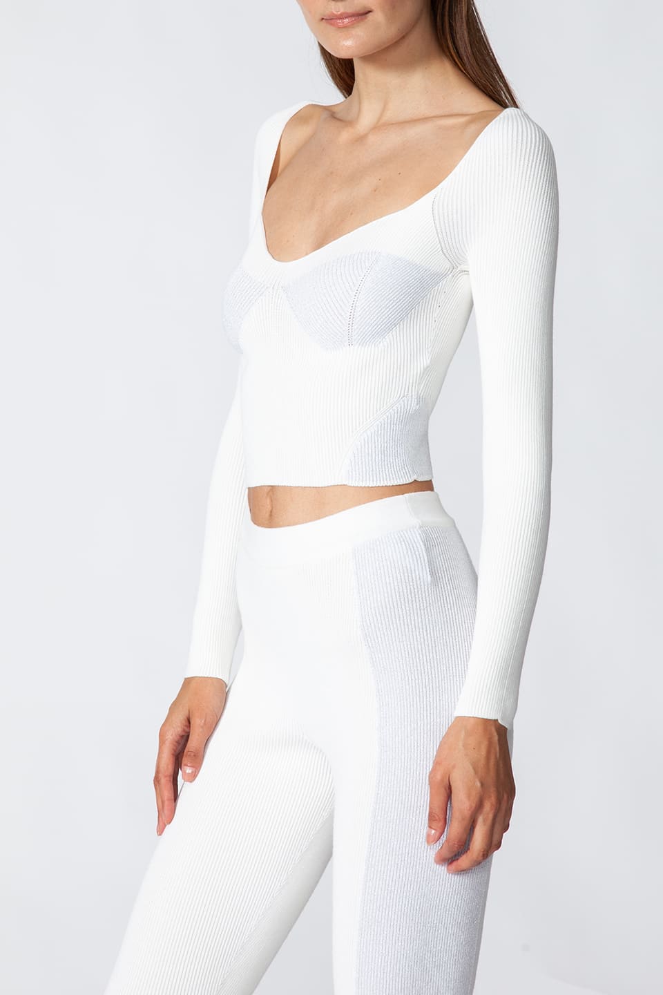 Model in pose from a side while wearing fashion artist Kukhareva London's trendy white top, with cut out neckline and inserts threaded with metallic, shimmering yarn.