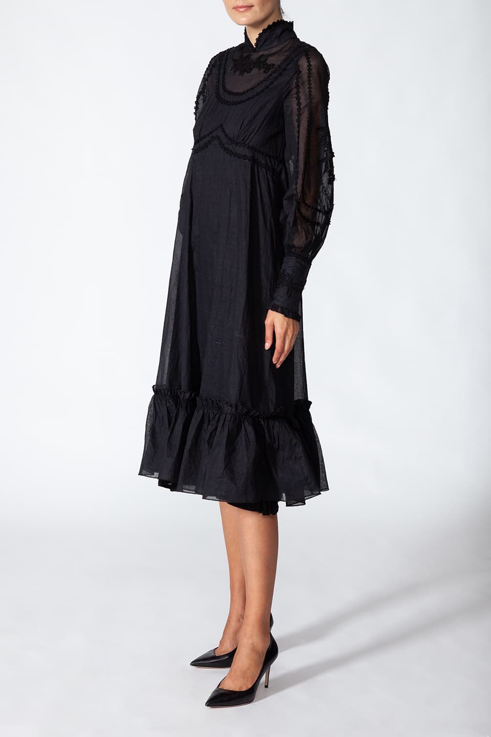 Thumbnail for Product gallery 3, Model wearing long black dress in cotton. with floral embroidery on the chest, in pose from right side. Dress is from Fashion Designer Manoush collection.