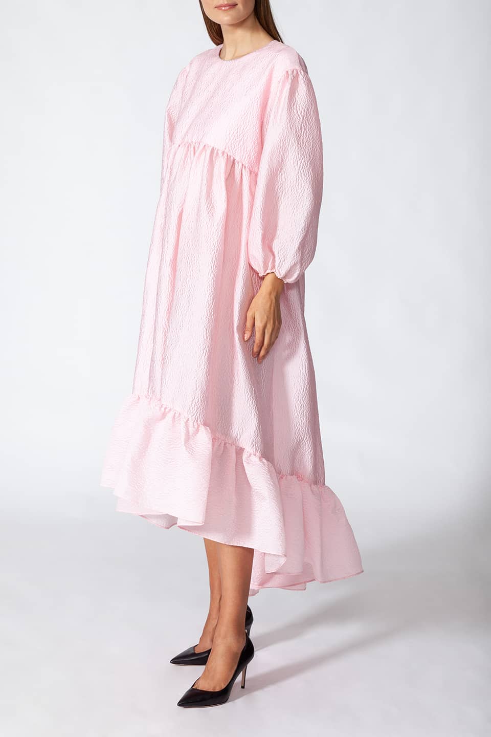Model in pose from right side wearing Manoush sylist pink long dress with puffy sleeves. Scalloped neck with contrasting stitching.